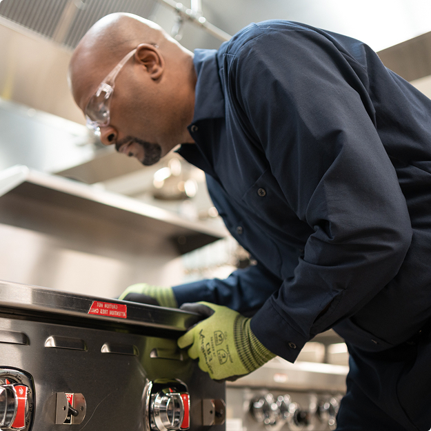 Technician leaning over a commercial range to adjust its control knobs