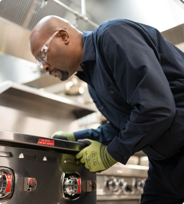 Technician leaning over a commercial range to adjust its control knobs