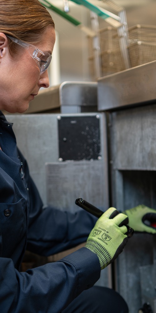 Facilities Management technician in work gloves servicing commercial kitchen equipment