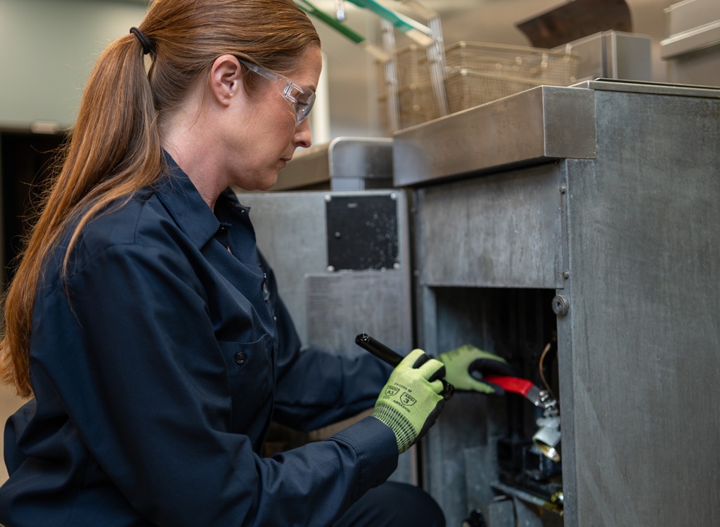 Facilities Management technician in work gloves servicing commercial kitchen equipment