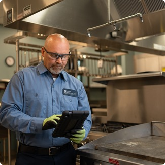 Facilities Management technician reviewing a service tablet in a commercial kitchen