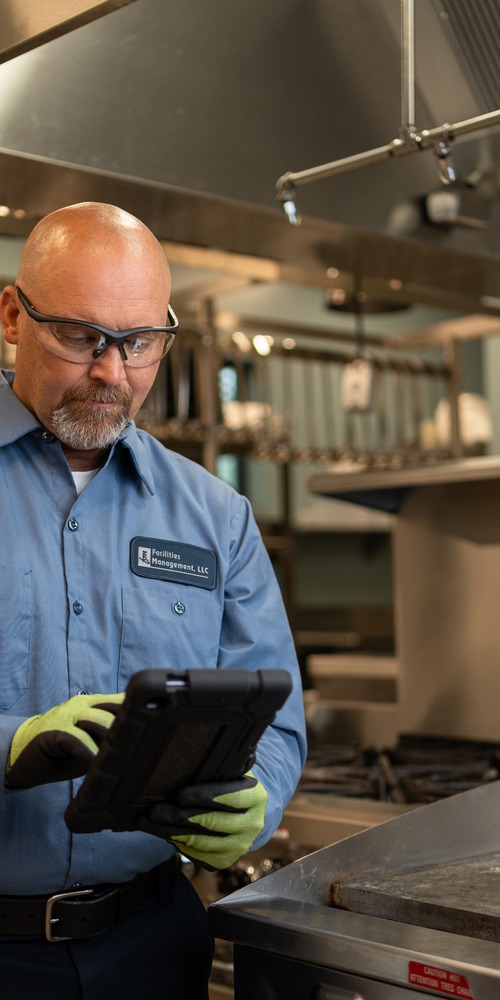 Facilities Management technician reviewing a service tablet in a commercial kitchen