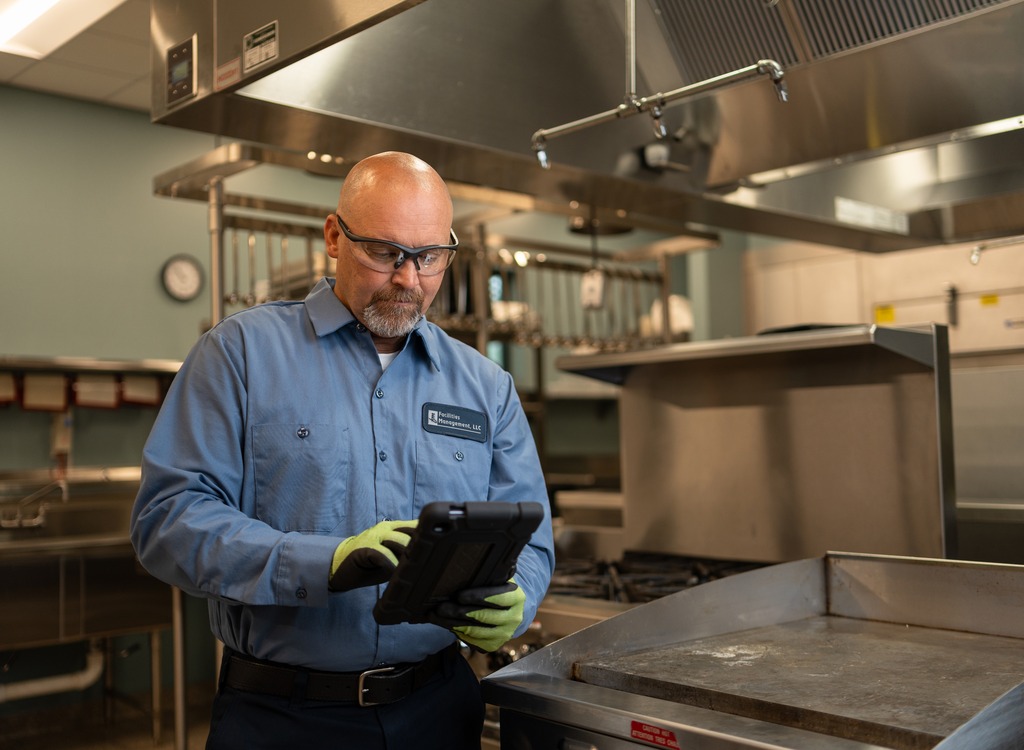 Facilities Management technician reviewing a service tablet in a commercial kitchen