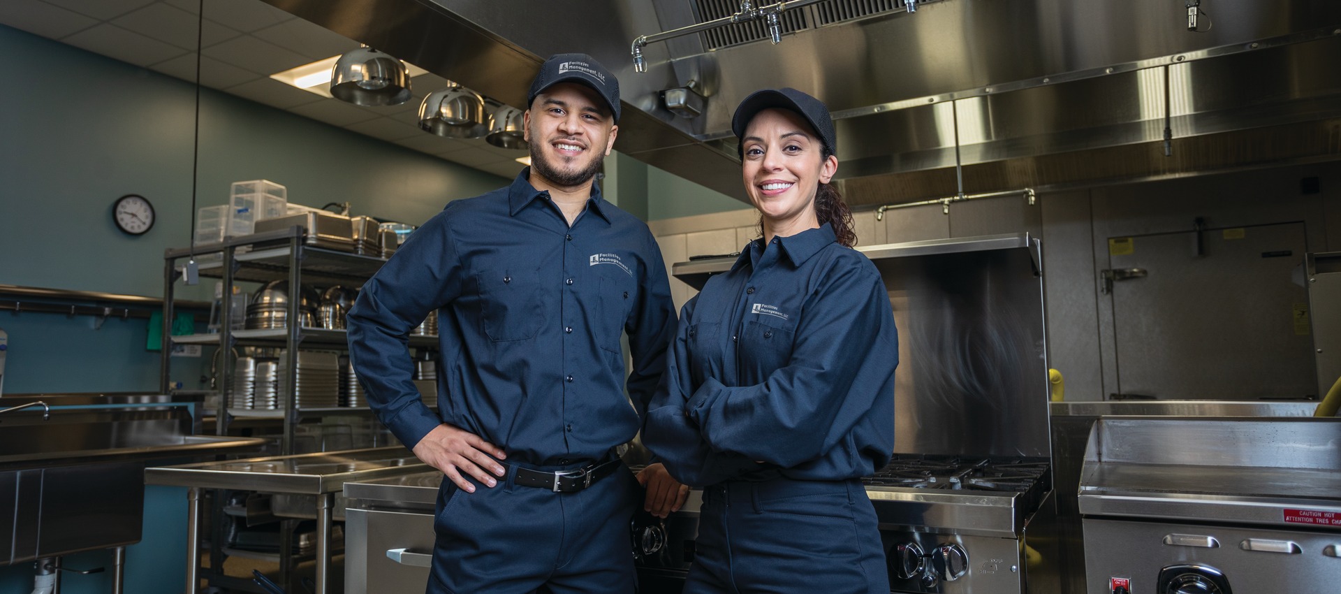 Two Facilities Management technicians in uniform standing in a commercial kitchen