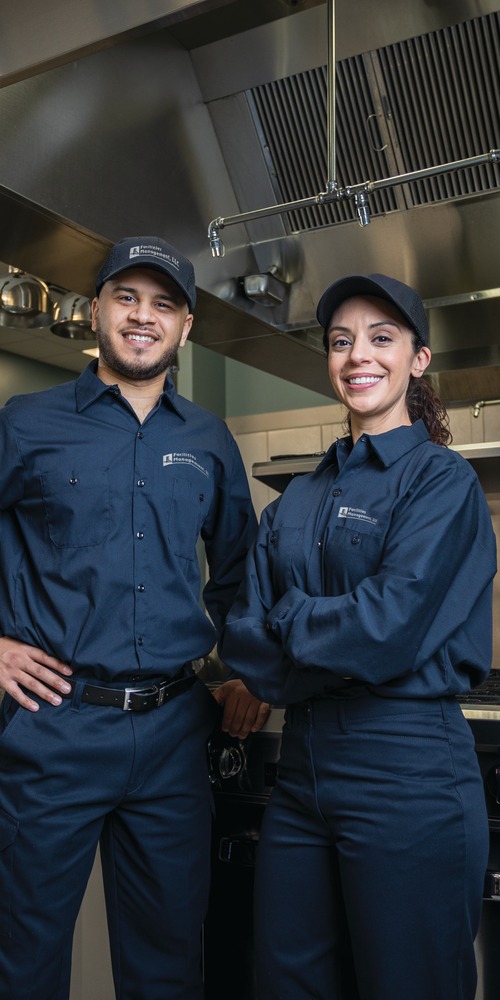 Two Facilities Management technicians in uniform standing in a commercial kitchen