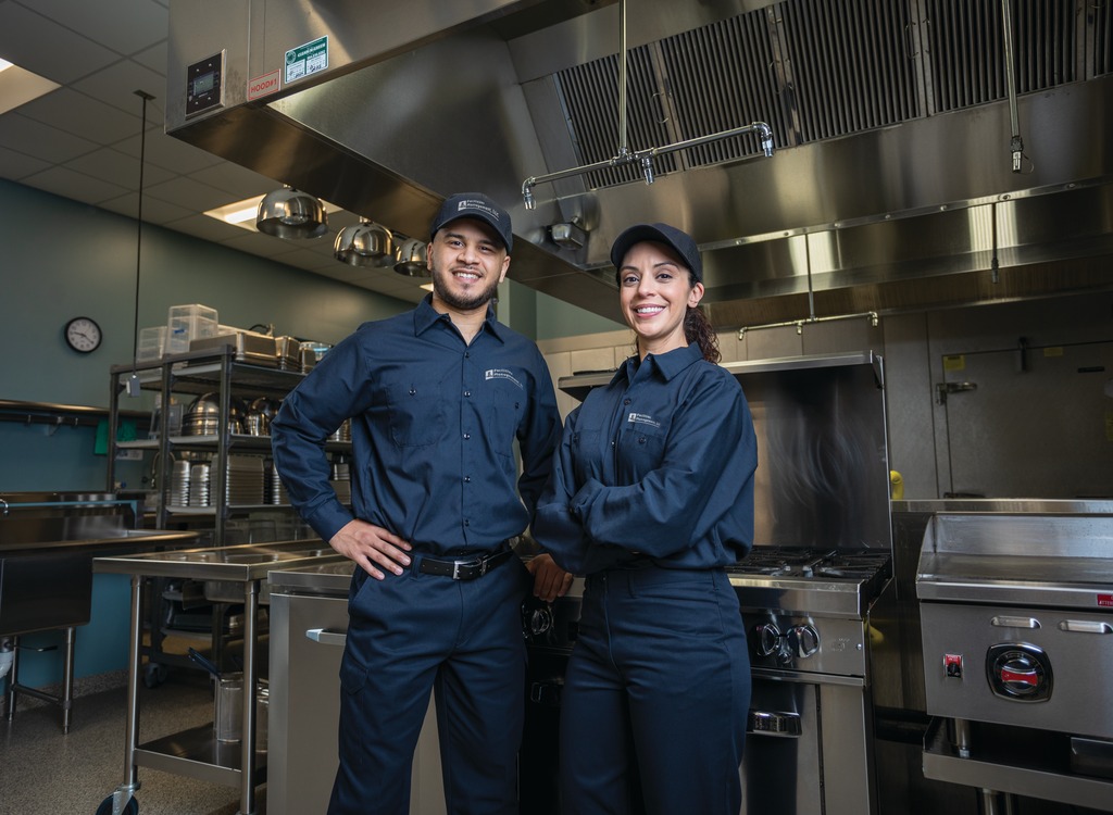 Two Facilities Management technicians in uniform standing in a commercial kitchen