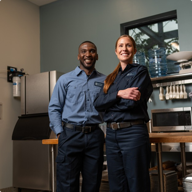 Two smiling Facilities Management team members standing with arms crossed in a break room