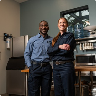 Two smiling Facilities Management team members standing with arms crossed in a break room