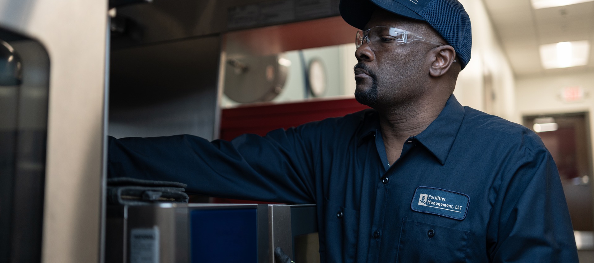 Facilities Management technician in a cap examining a commercial kitchen equipment cabinet