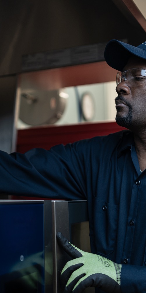 Facilities Management technician in a cap examining a commercial kitchen equipment cabinet