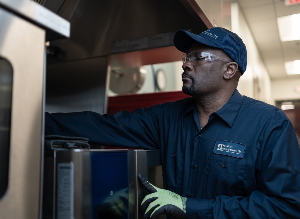 Facilities Management technician in a cap examining a commercial kitchen equipment cabinet