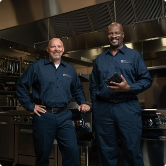 Two smiling Facilities Management technicians standing in a commercial kitchen
