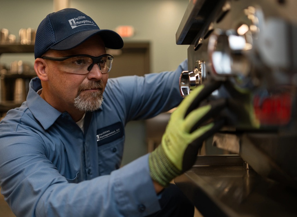 Facilities Management technician in a cap repairing commercial foodservice equipment