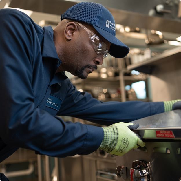 Facilities Management technician in a cap adjusting a control on commercial cooking equipment