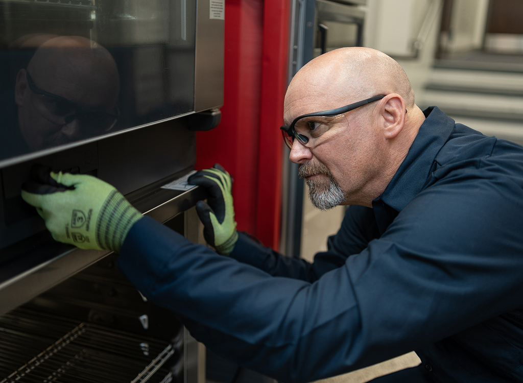 Technician in safety glasses inspecting a commercial oven door