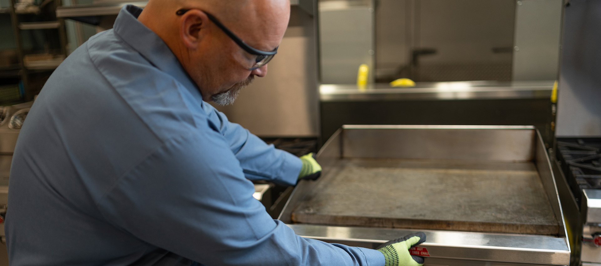 Technician in work gloves servicing a commercial flat-top griddle