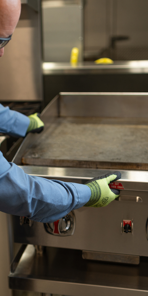 Technician in work gloves servicing a commercial flat-top griddle