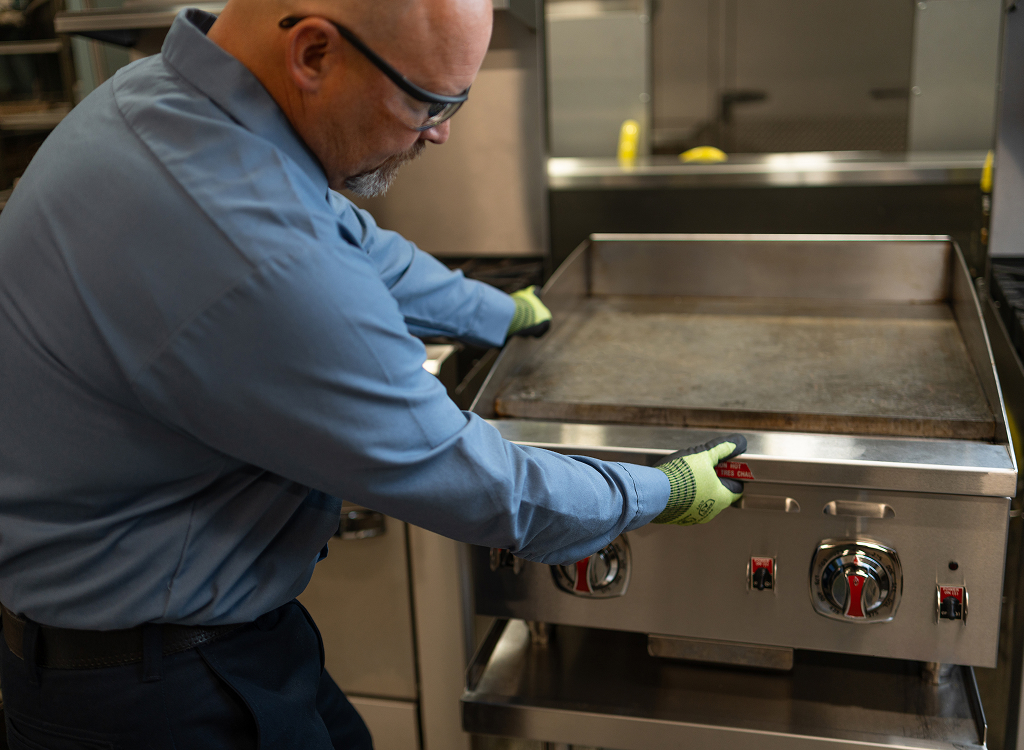 Technician in work gloves servicing a commercial flat-top griddle